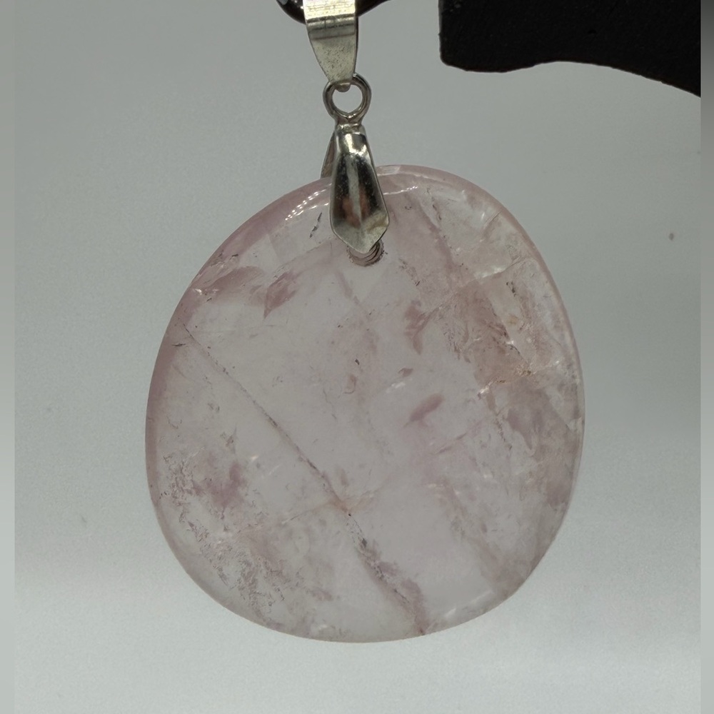 A polished rose quartz pendant with natural internal fractures.
